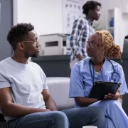 Uma profissional de saúde e um paciente, ambos negros e jovens. Autora trata do programa de saúde da população negra, o PNSIPN