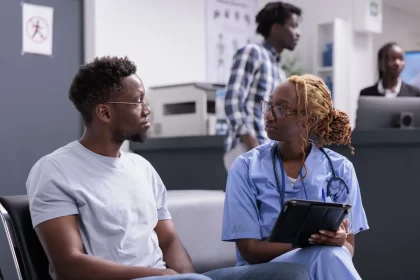 Uma profissional de saúde e um paciente, ambos negros e jovens. Autora trata do programa de saúde da população negra, o PNSIPN