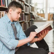 Aluno sentado no chão de uma biblioteca lendo um livro. Autor fala do seu mundo de introspecção