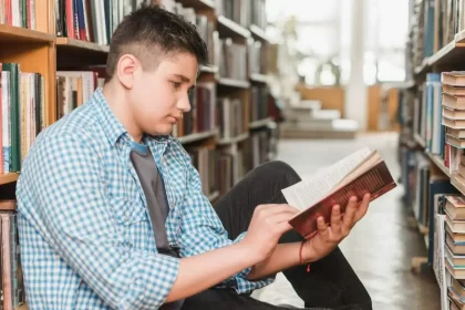 Aluno sentado no chão de uma biblioteca lendo um livro. Autor fala do seu mundo de introspecção
