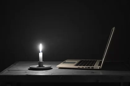 Um laptop sobre a mesa com uma vela acesa. Luz só da vela.
