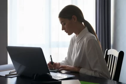 Uma mulher sentada à mesa, escrevendo num laptop. Autora fala de seu desejo de escrever romance